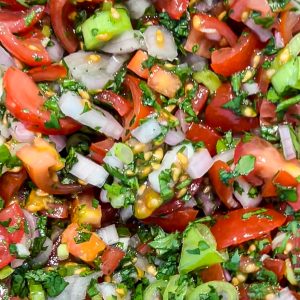 Close-up of a colorful fresh salsa mix, featuring chopped tomatoes, onions, cilantro, and green peppers, with visible seeds and a glossy texture. The vibrant ingredients are finely diced and blended, creating a fresh and appetizing appearance.