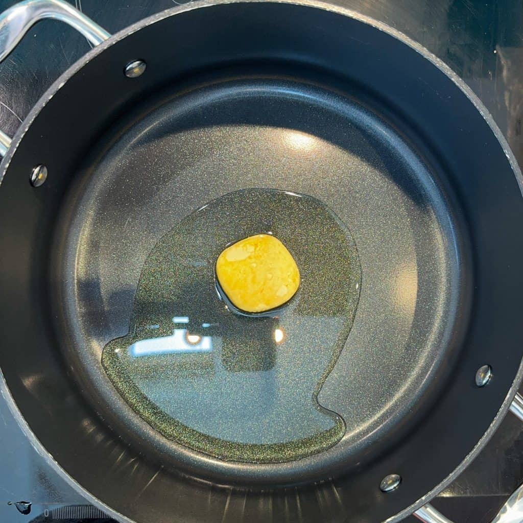 A black frying pan on a stovetop with a single piece of butter melting in the center, creating a small pool of melted butter.