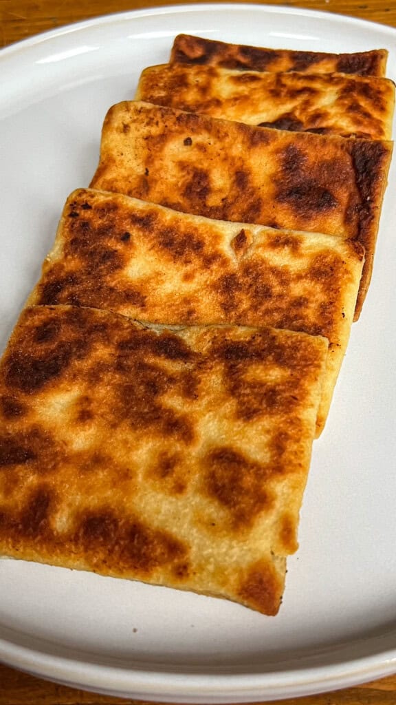 Four rectangular, golden-brown potato scones are neatly arranged in a row on a plain white plate, showing a crispy and evenly browned surface.