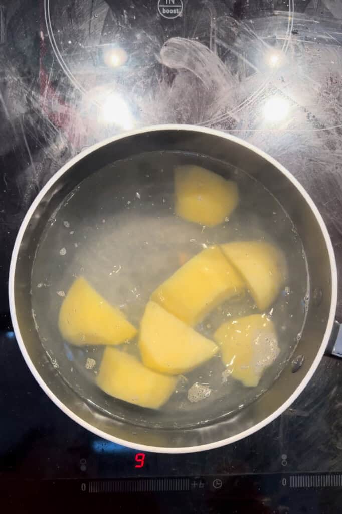 A pan of water with several peeled and chopped potatoes boiling on a hob, with the heat setting showing 9 on the digital display.