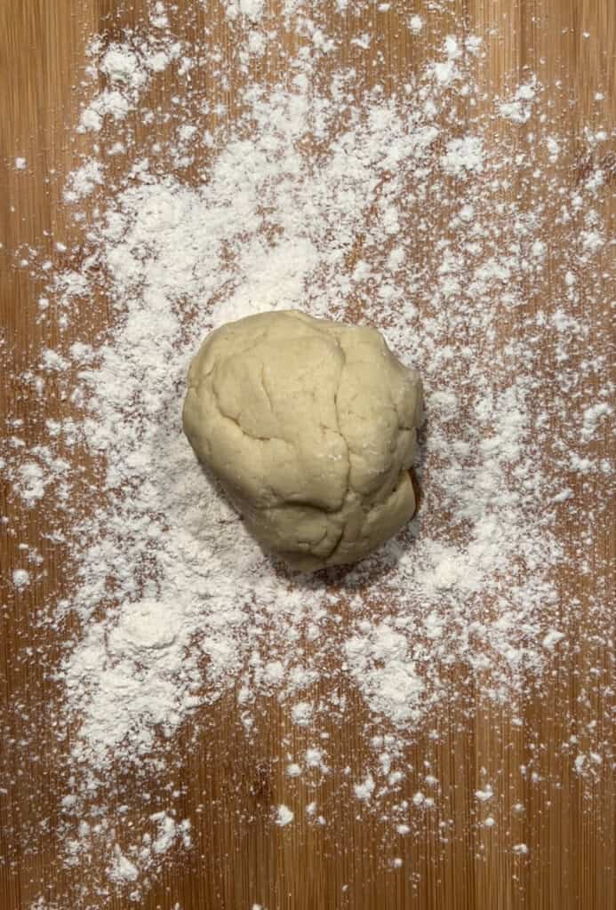 A ball of dough resting on a wooden surface sprinkled with flour.