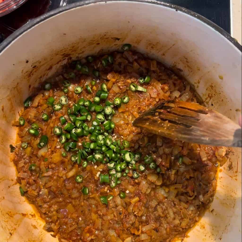 adding chopped chillis into pot with onions and spices