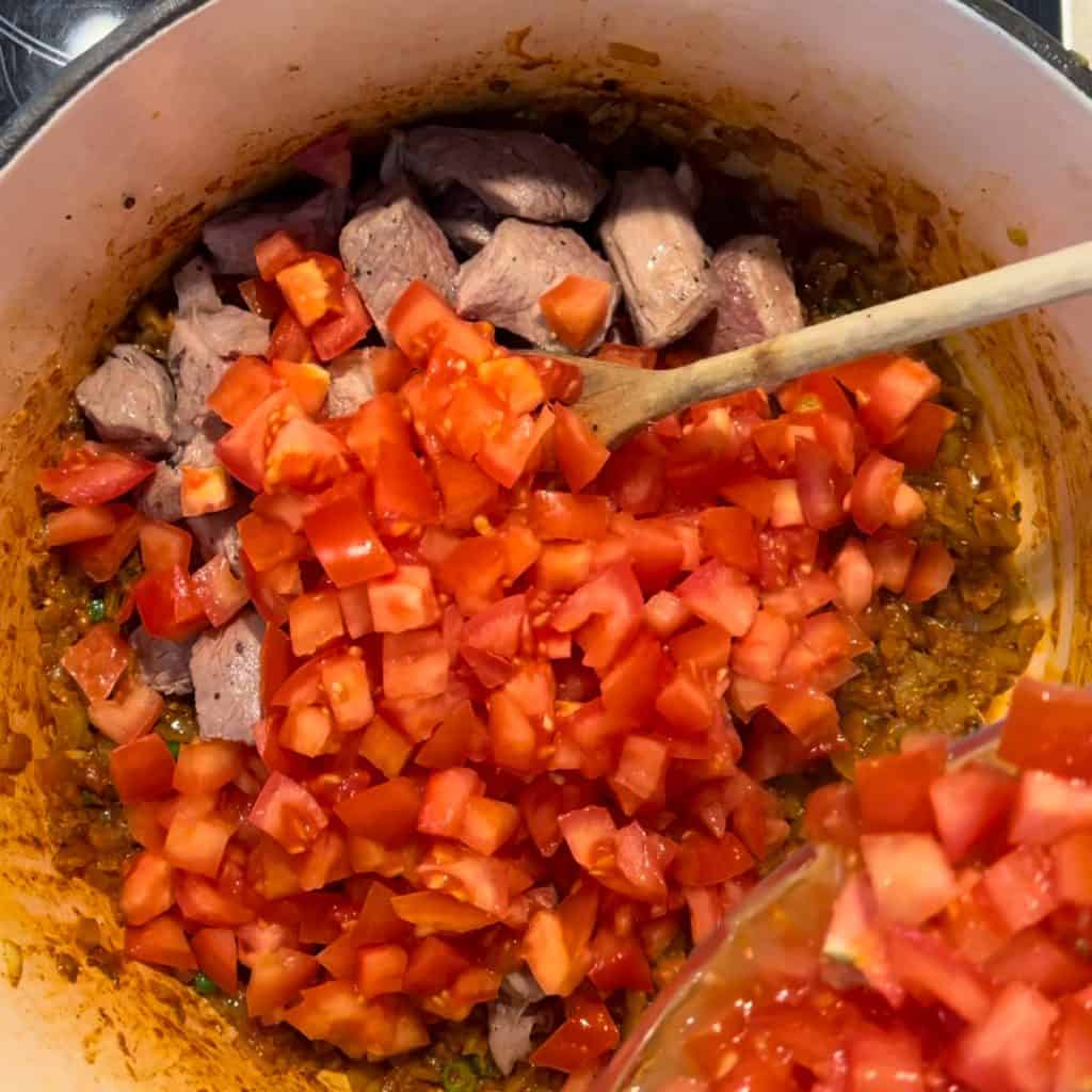 adding chopped tomatoes and lamb into pot