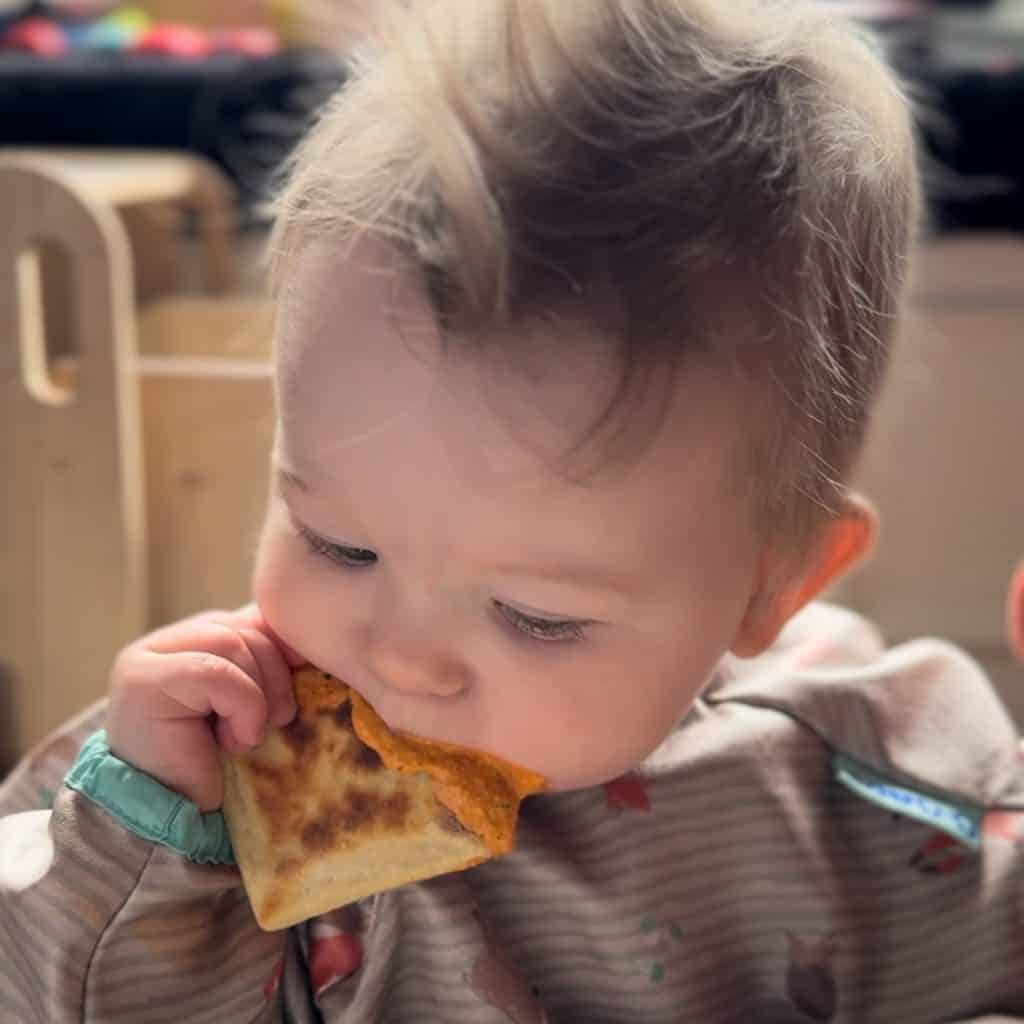 baby eating potato scone dipped in goats cheese romesco