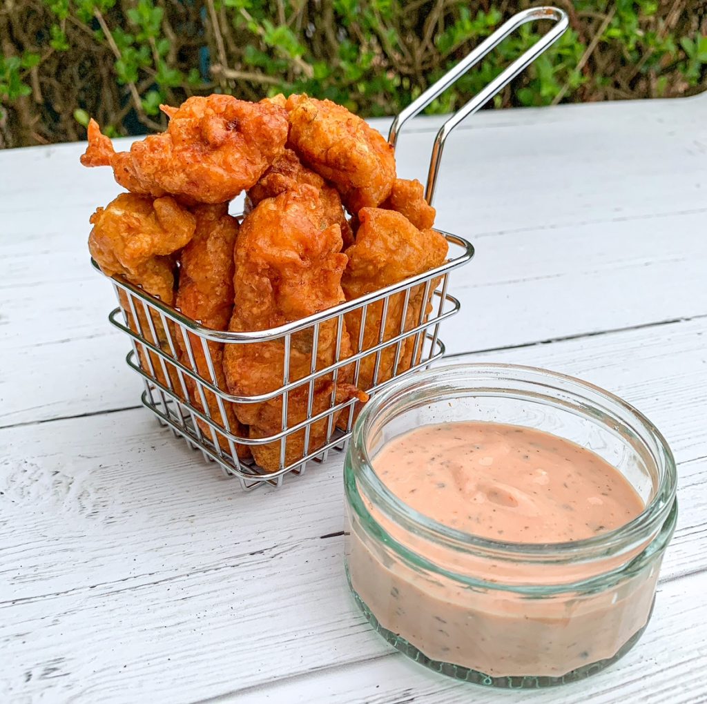 chicken pakora in a wire basket on a table beside dipping sauce