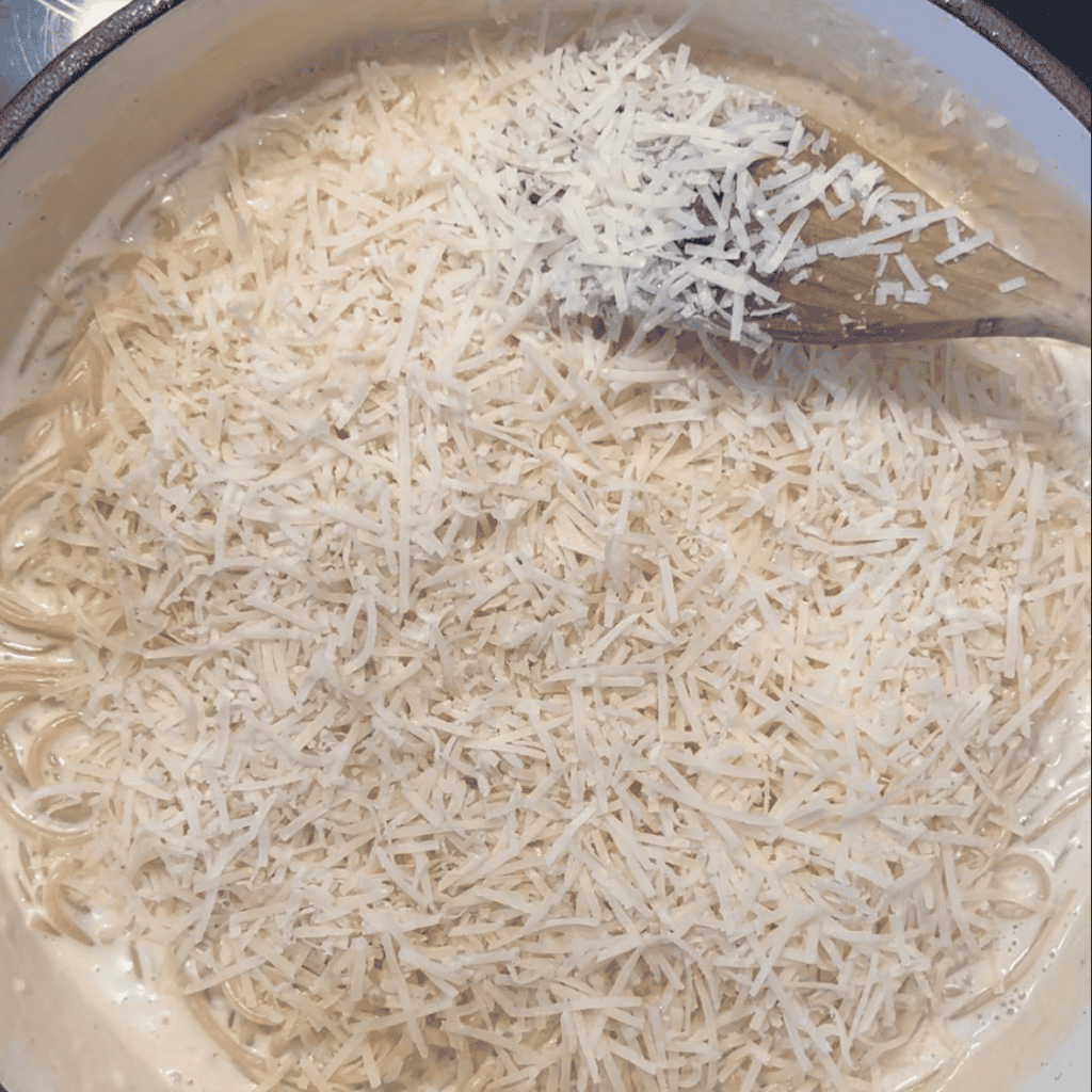 a thick layer of grated parmesan on top of Alfredo pasta in a pan