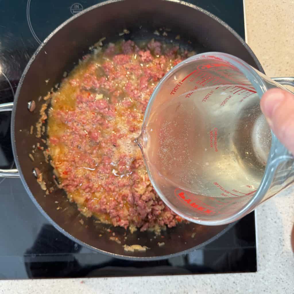 pouring Prosecco into pan with Italian sausage