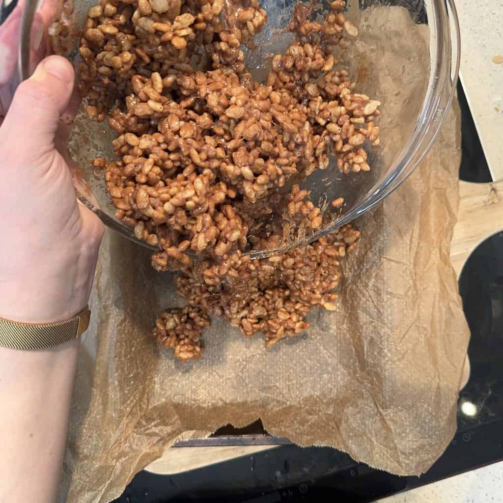 Two sticks of butter melting in a clear glass bowl placed on a black stovetop, viewed from above. The butter is beginning to soften and create a slick surface in the base of the bowl. The stovetop surface is partially visible.