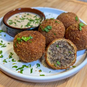 haggis bon bons on a plate sprinkled with fresh parsley beside a ramekin of whisky sauce