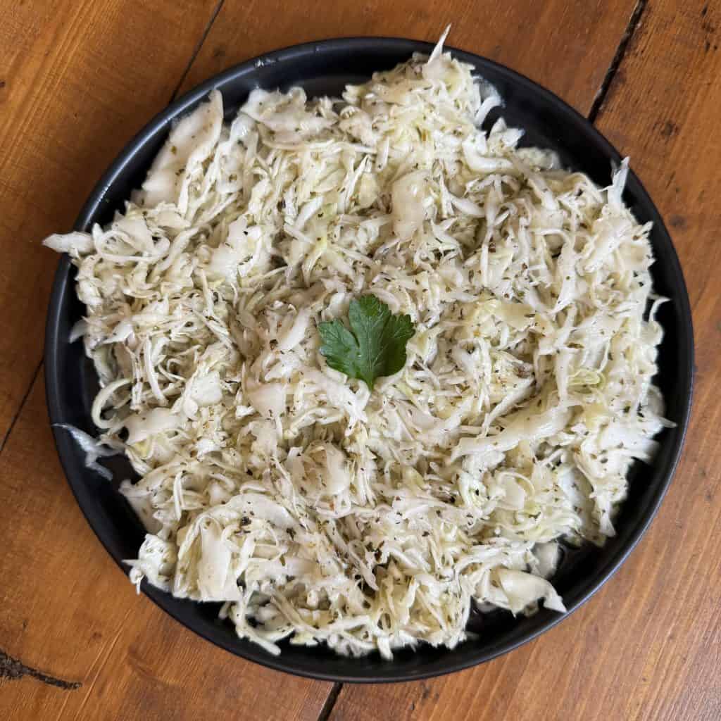 A black bowl filled with shredded cabbage salad, garnished with a single parsley leaf, sits on a wooden table.