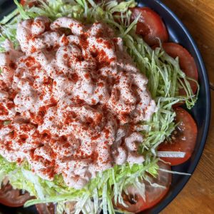 A salad with a base of shredded lettuce and sliced tomatoes. Topped with a creamy pink dressing, generously sprinkled with paprika. Served on a dark plate.