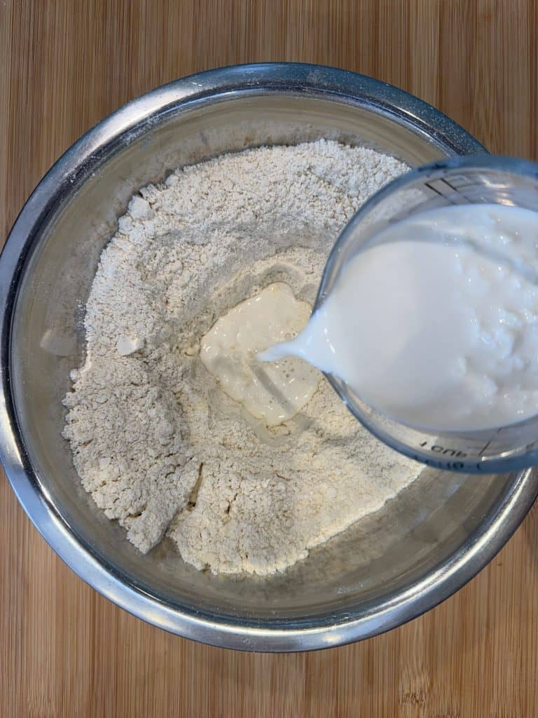 A batch of freshly baked scones with raisins is arranged on a baking tray lined with parchment paper. The scones are golden brown and evenly spaced, showcasing a flaky, textured surface.