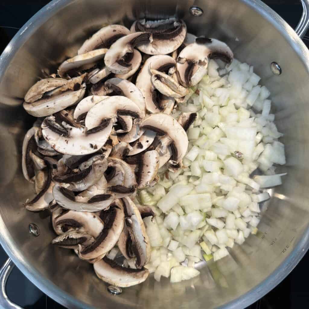 Chopped onions and sliced mushrooms are placed in a large stainless steel pot, ready for cooking.