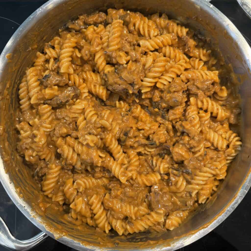 A pot filled with creamy beef and rotini pasta, coated in a rich, brown sauce. The pasta is well mixed, and chunks of beef are visible, suggesting a hearty and savory dish.