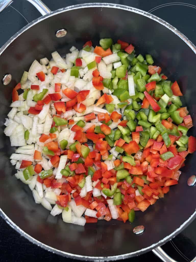 Chopped onions, red bell peppers, and green bell peppers in a large pot, ready for cooking.