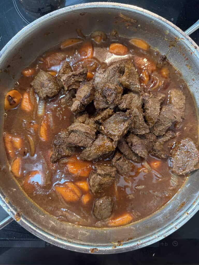 A pot filled with a rich, brown stew featuring chunks of tender beef, sliced carrots, and onions simmering in a thick gravy.
