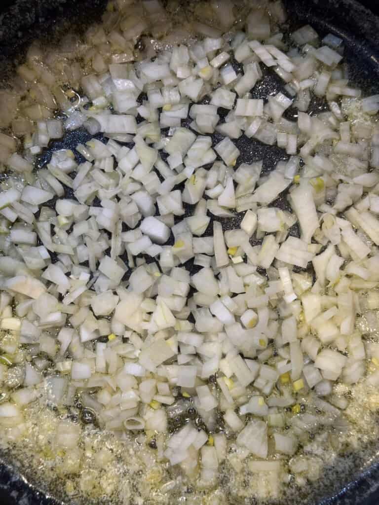 Close-up of chopped onions being sautéed in a pan with melted butter, beginning to soften and turn translucent.