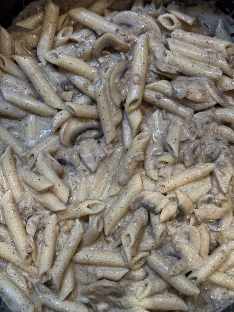 Creamy penne pasta mixed with sliced mushrooms in a rich, peppery sauce. The pasta and mushrooms are evenly coated, creating a hearty and savory dish.