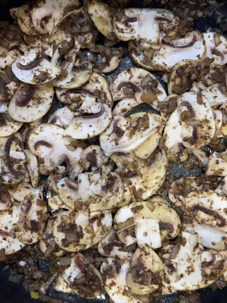 Sliced mushrooms and diced onions are being sautéed together in a pan, seasoned with spices, and beginning to brown.