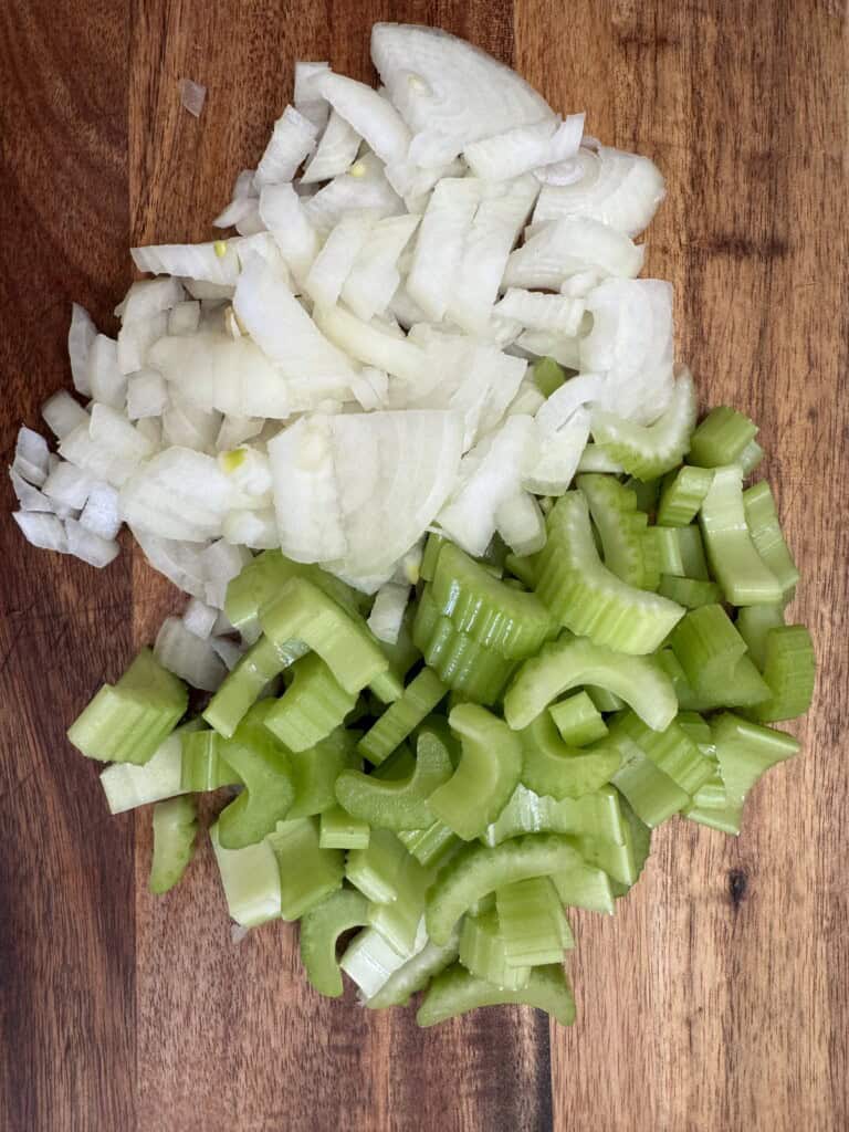 Chopped white onions and sliced celery arranged on a wooden cutting board.