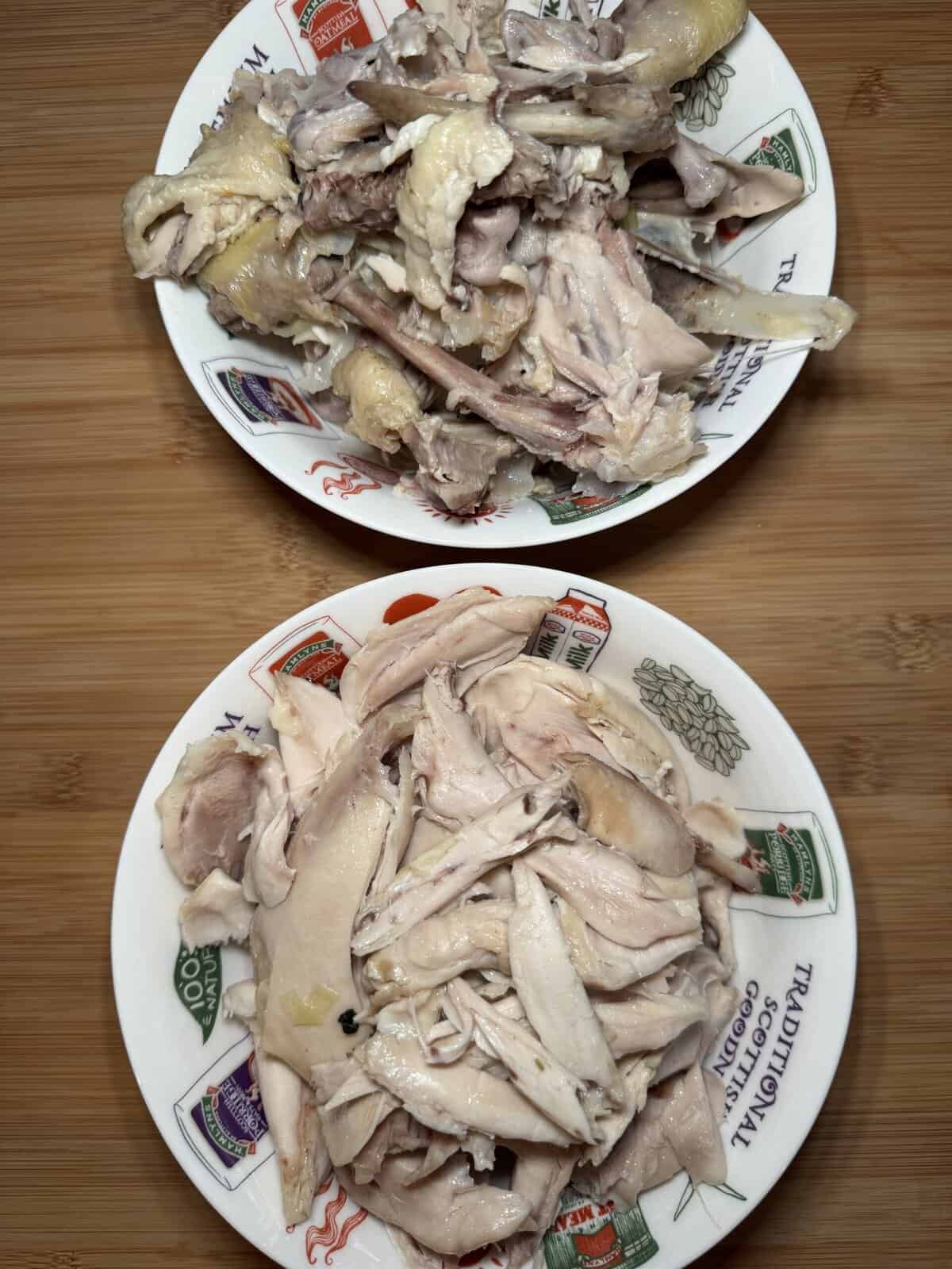Two bowls of cooked, shredded chicken are placed on a wooden surface. The chicken in the top bowl includes skin and bones, while the chicken in the bottom bowl is boneless and more uniformly shredded.