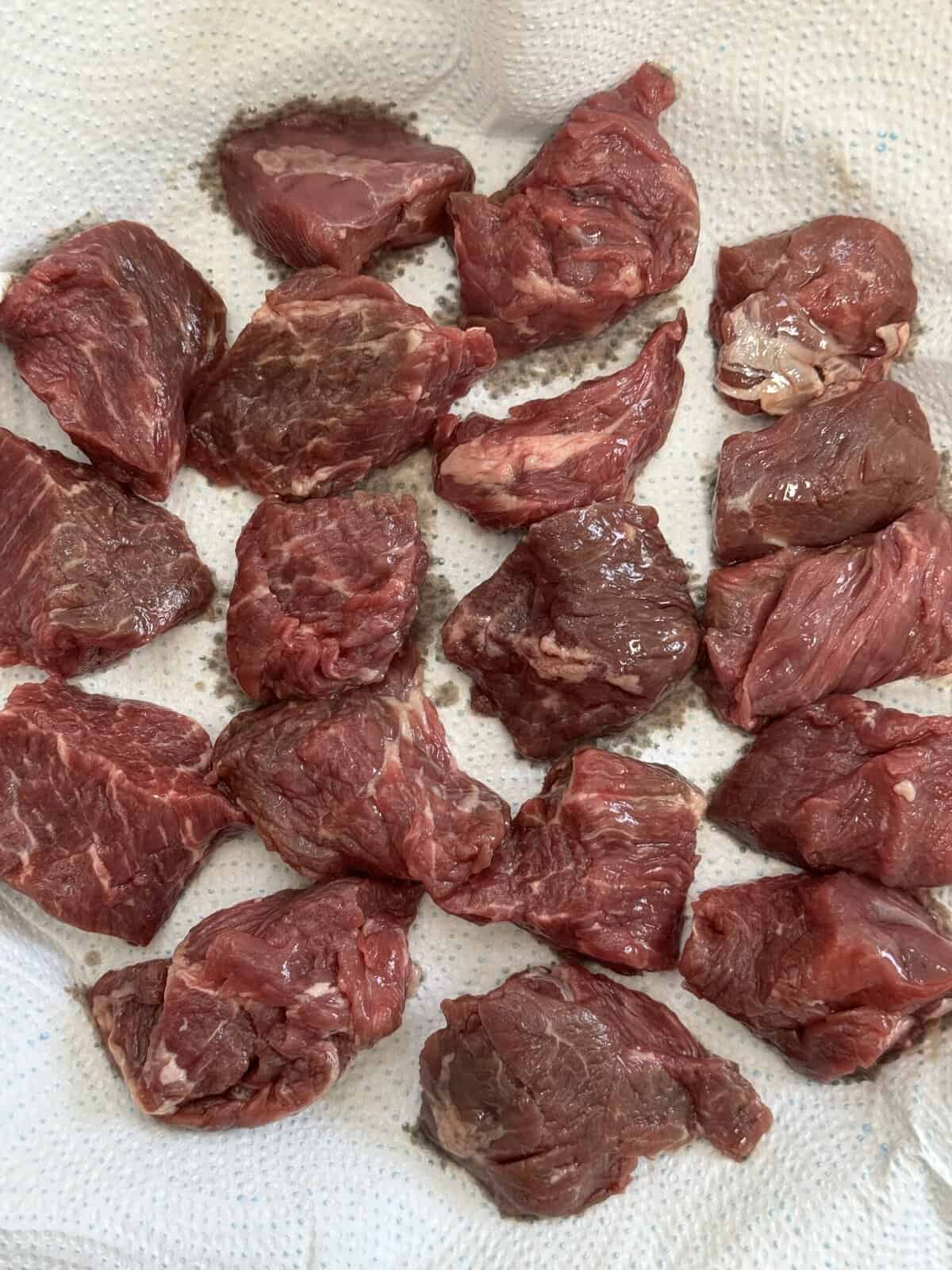 Chunks of raw chucks eye beef placed on white paper towels, arranged in neat rows and spaced apart, with visible marbling and moisture on the meat.