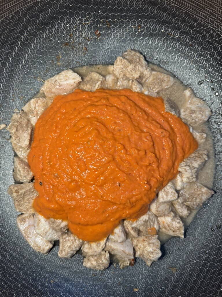Cooked chunks of meat arranged in a circle on a dark, patterned plate, topped with a generous amount of bright orange-red sauce in the center.