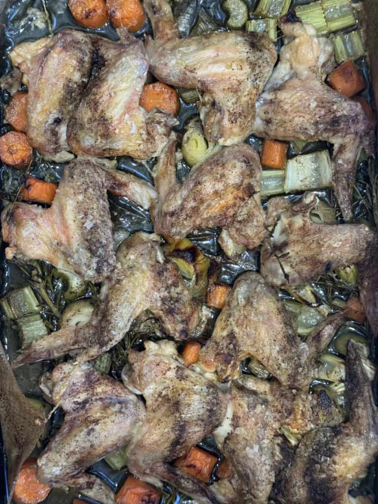 A baking tray filled with roasted chicken wings, seasoned and cooked with pieces of carrot and celery, all browned and baked together.