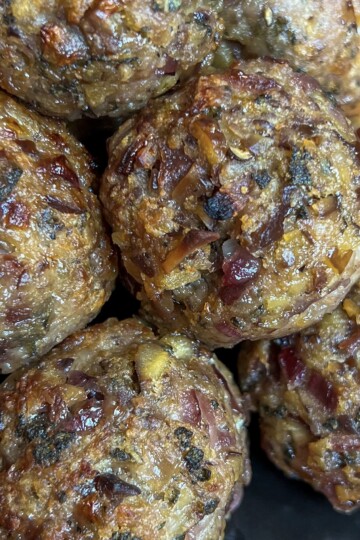 Close-up of several cooked sausage meat stuffing balls containing visible pieces of herbs, onions, and possibly cheese, showing a textured and slightly browned surface.