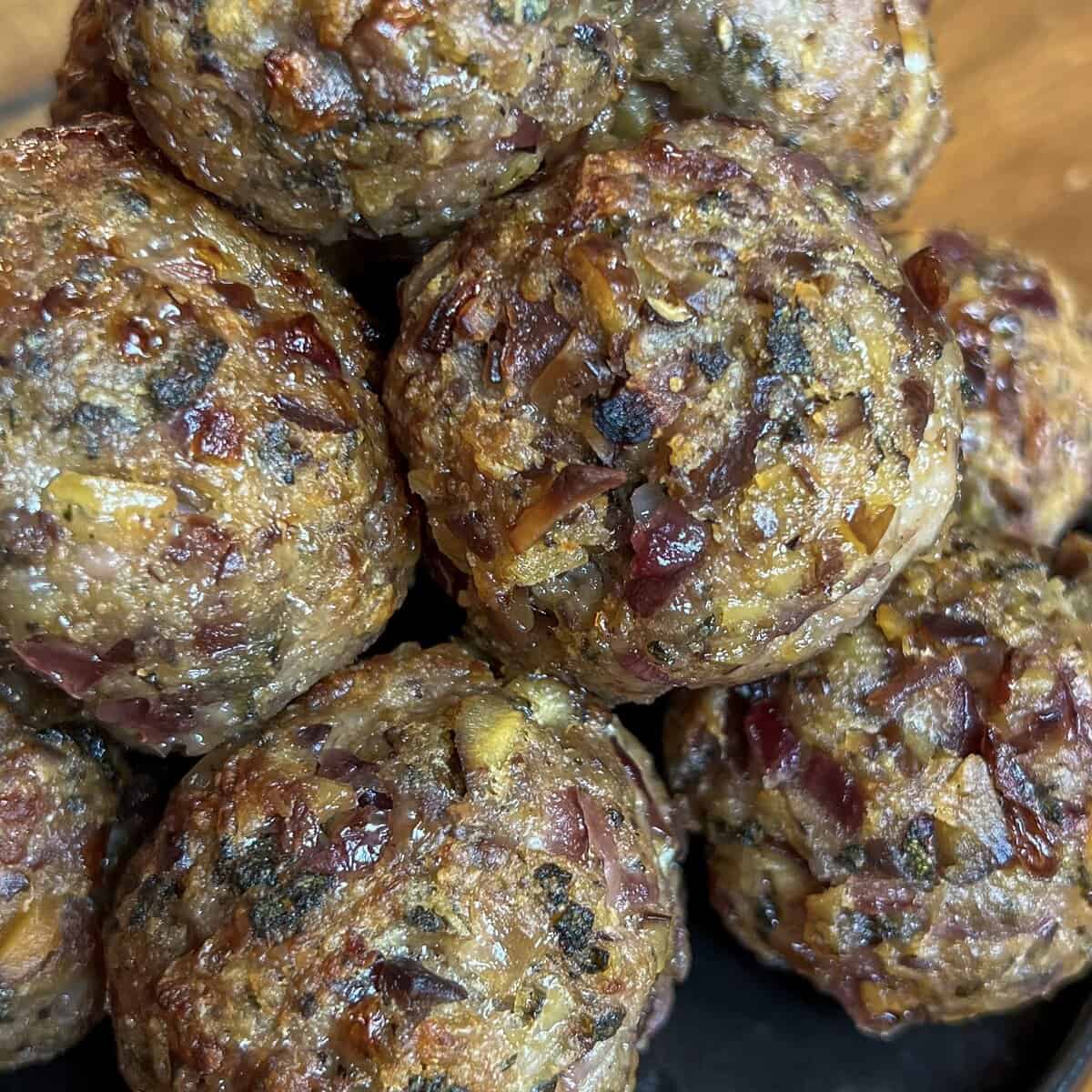 Close-up of several cooked sausage meat stuffing balls containing visible pieces of herbs, onions, and possibly cheese, showing a textured and slightly browned surface.
