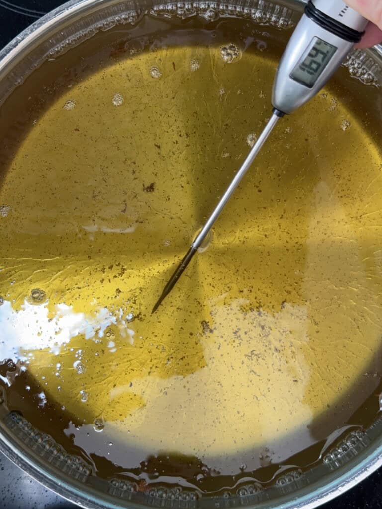 A close-up of a pot filled with hot oil being measured with a digital thermometer, which displays a temperature of 369°F.