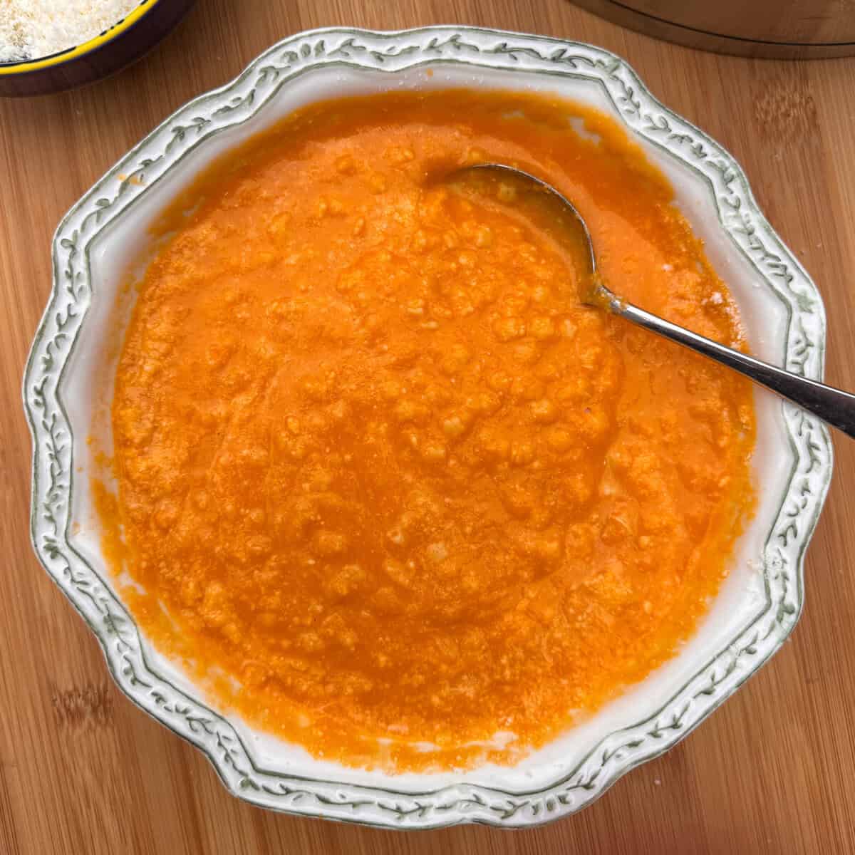 A decorative bowl filled with Italian penicillin soup (pasting) with a slightly chunky texture, and a silver spoon resting inside.
