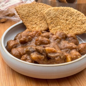 A bowl of thick Scottish stovieswith visible chunks of meat and vegetables, served with two large, crispy wholegrain crackers on a wooden surface.