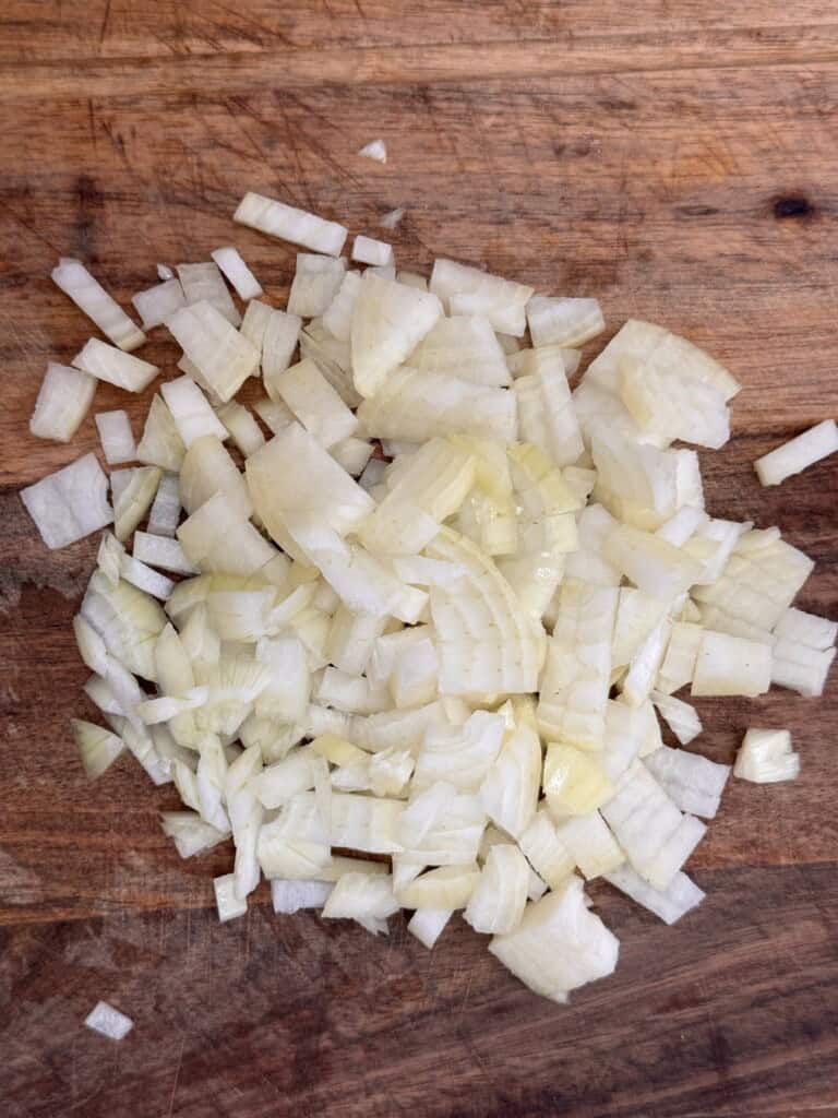 Chopped white onion pieces on a wooden chopping board.