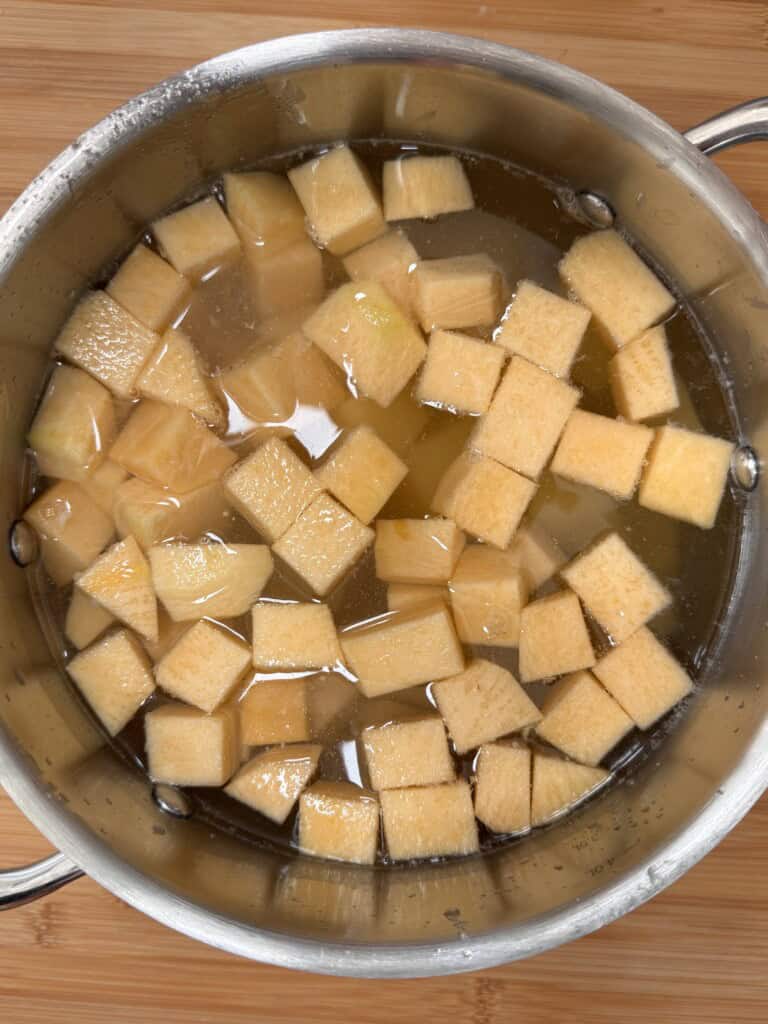 A stainless steel saucepan filled with water and chunks of peeled, cubed swede, placed on a wooden surface.
