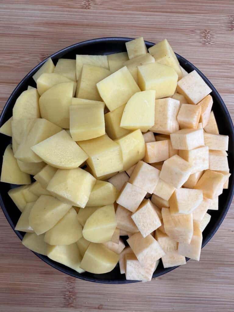 A black bowl filled with chopped yellow potatoes and cubed swede, placed on a wooden surface.