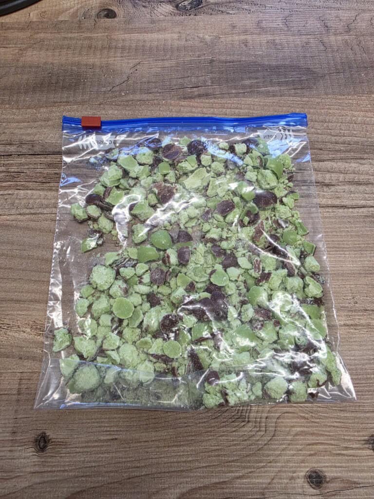 A clear zip-lock bag filled with small, broken pieces of mint aeros, placed on a wooden surface.