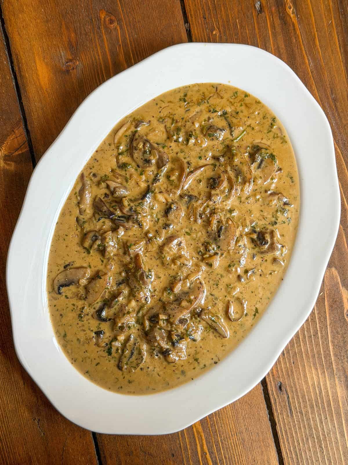 Oval white plate filled with Diane sauce, garnished with herbs, placed on a wooden table.