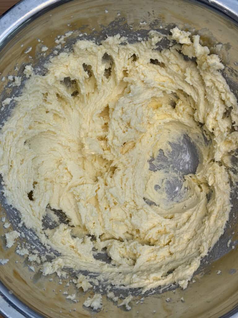 Creamed butter and sugar mixture in a metal mixing bowl, showing a light, fluffy texture with swirls made by a spoon or mixer.