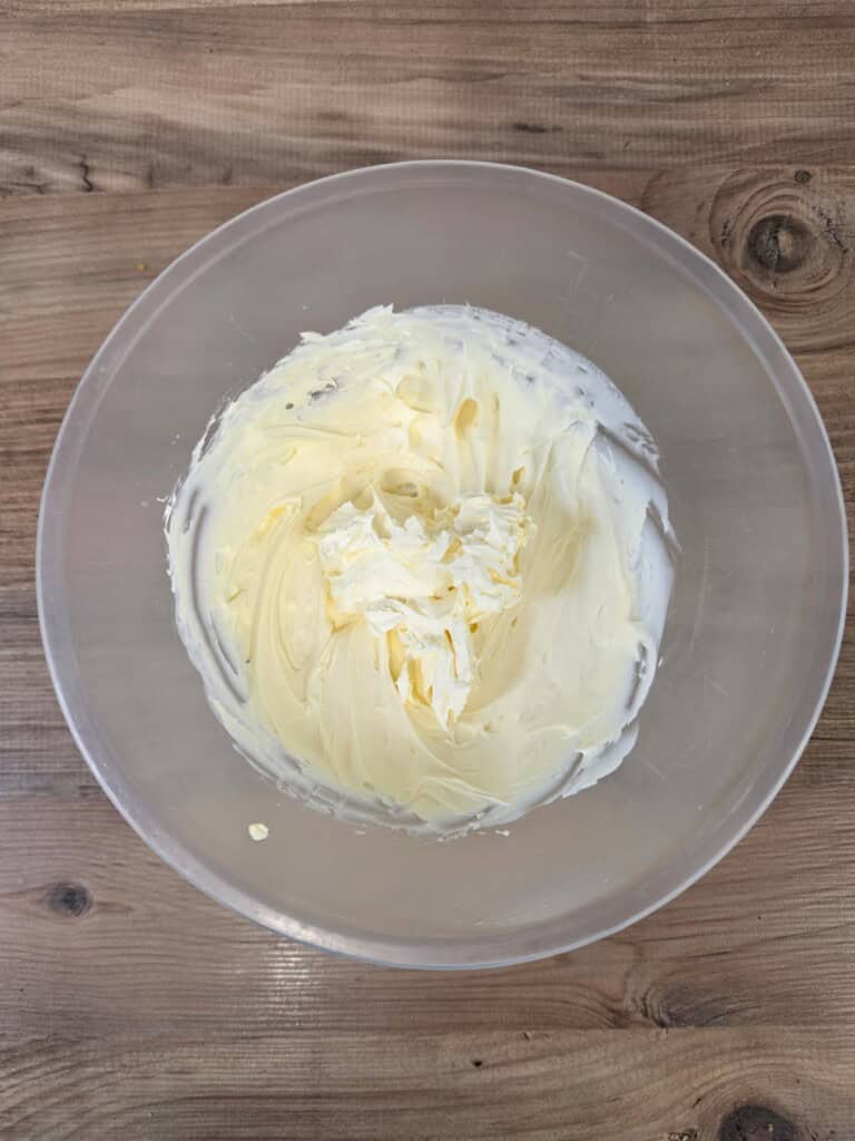 A clear bowl filled with creamy, whipped butter on a wooden surface.