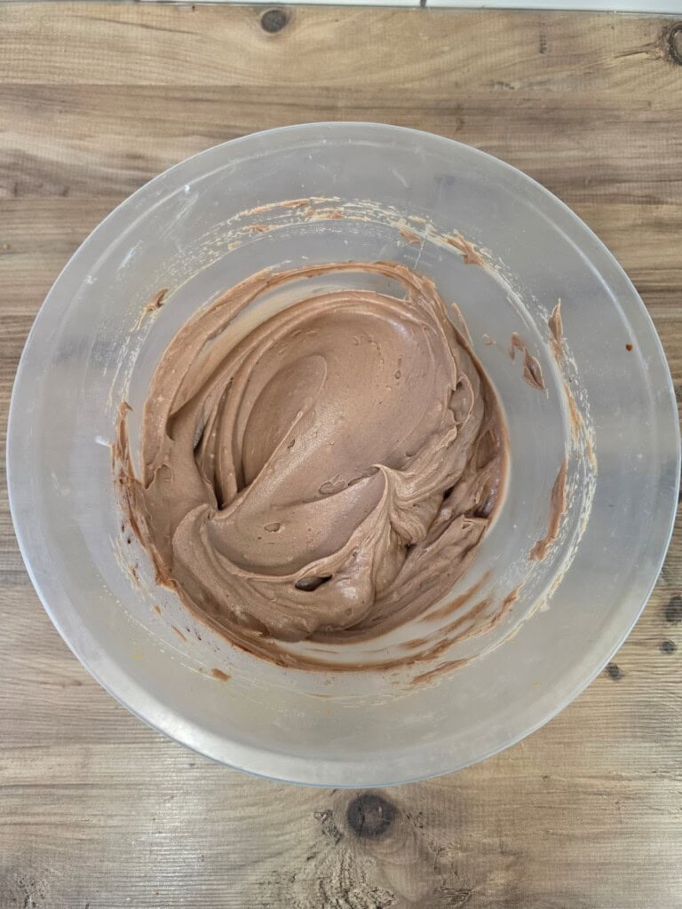 A clear mixing bowl filled with smooth, light brown chocolate mixture sits on a wooden surface.