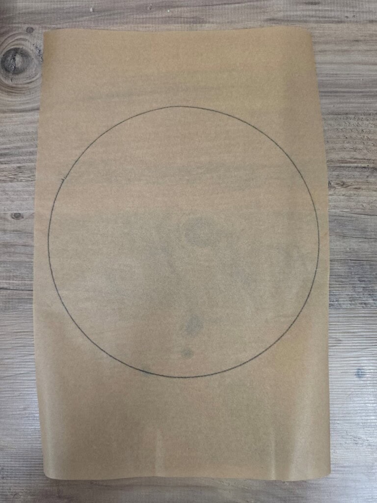 A large circle is drawn in pencil on a sheet of brown parchment paper, which is placed on a wooden surface.