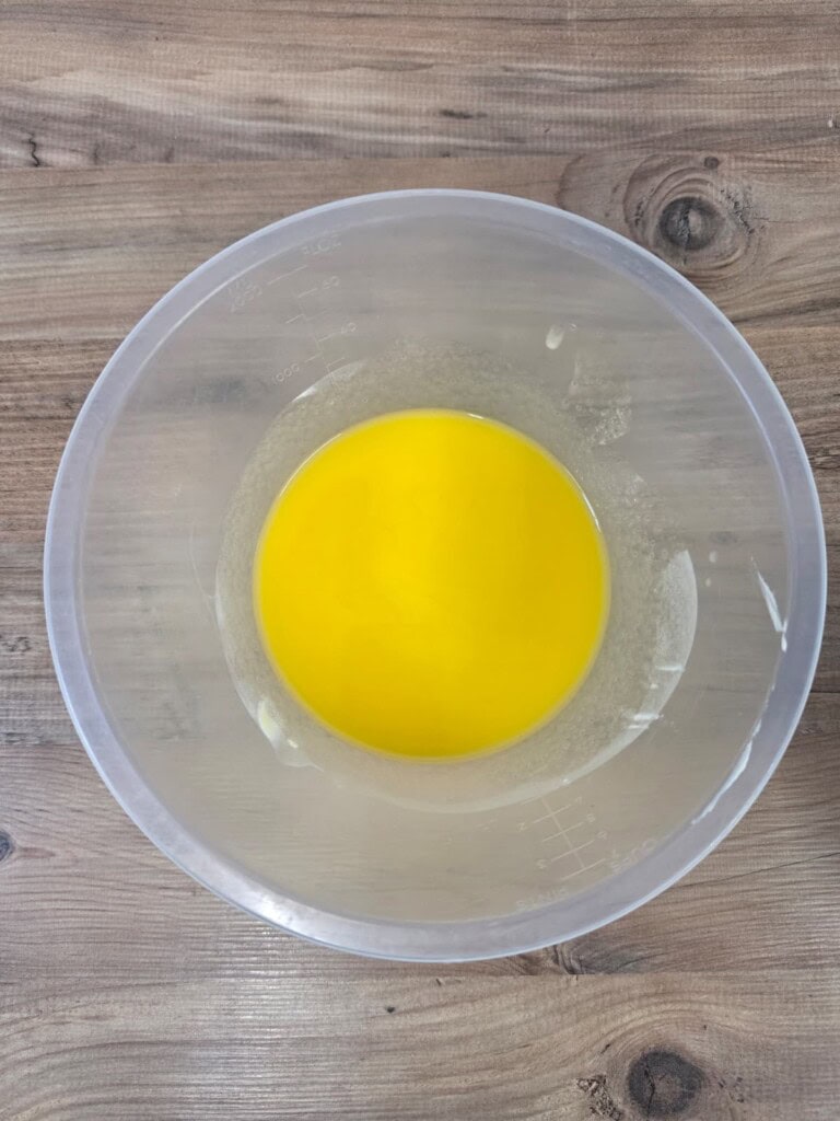 A clear plastic bowl with melted yellow butter sits on a wooden surface.