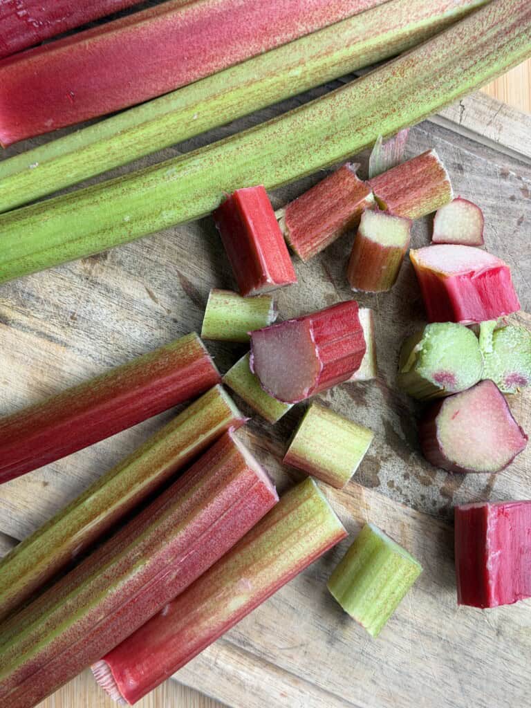 Sliced and whole rhubarb stalks, both red and green, are arranged on a wooden chopping board.