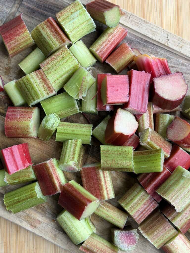 Chopped pieces of fresh rhubarb, both green and red, are spread out on a wooden chopping board.