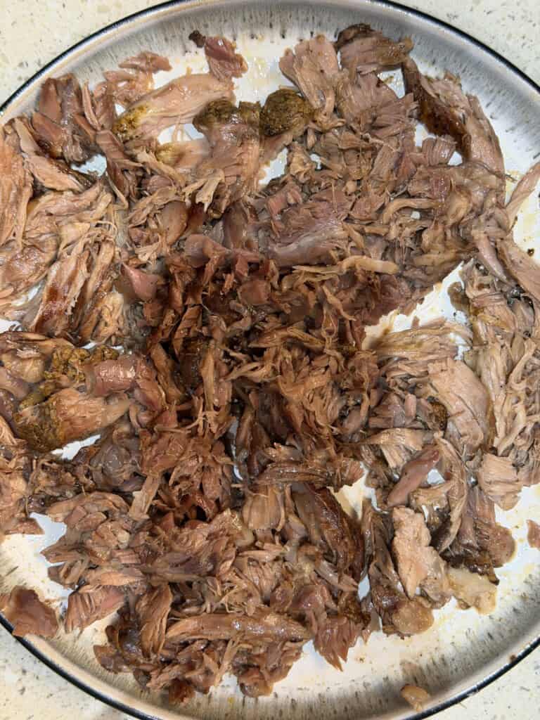 A plate filled with shredded, cooked lamb, spread out across the surface. The meat appears tender and juicy, with some pieces slightly browned.