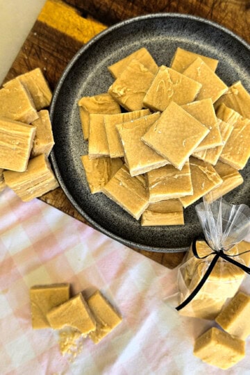 A plate of classic Scottish tablet pieces on a wooden board, with more tablet scattered around and some wrapped in a clear bag tied with a black ribbon.