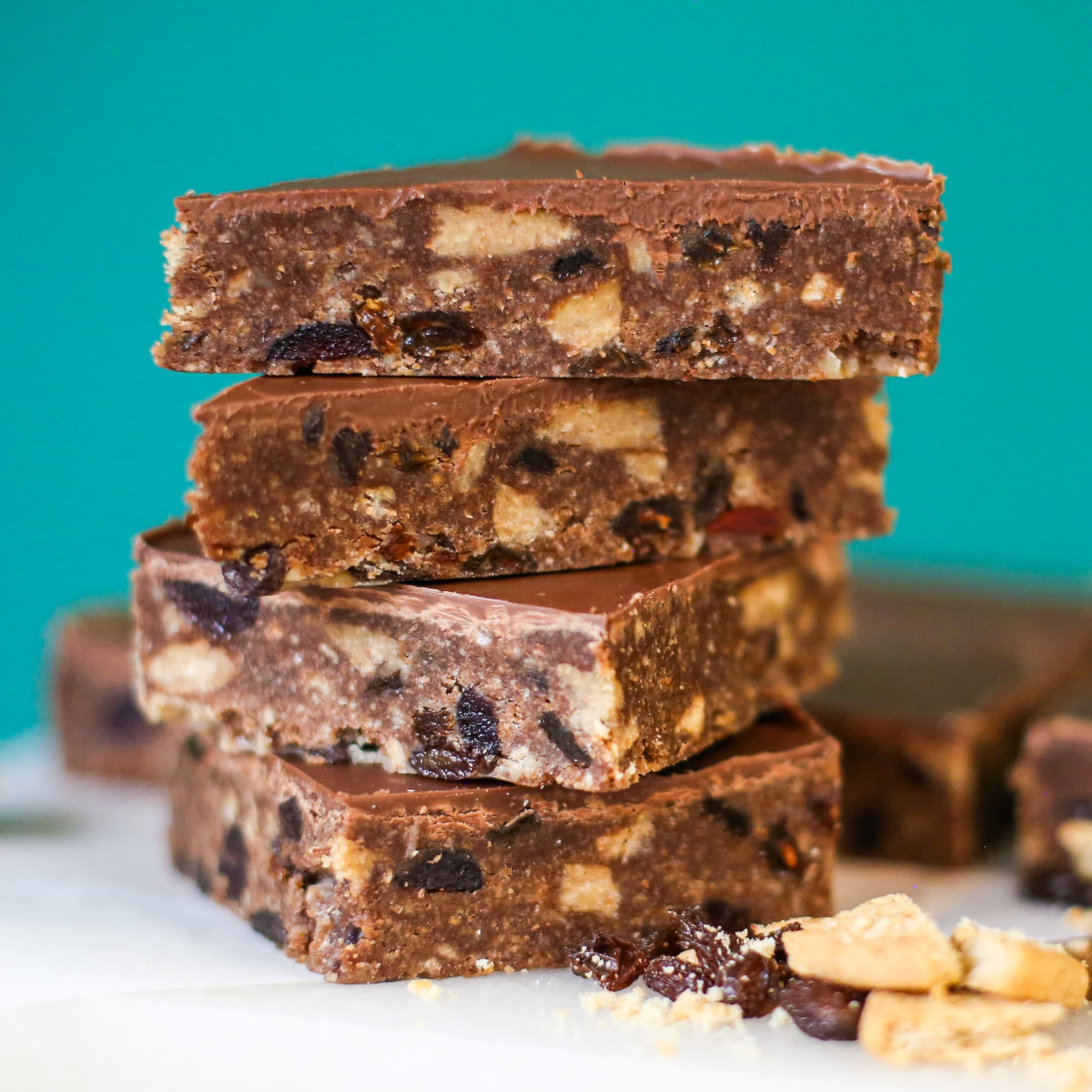 A stack of four chocolate tiffin bars with visible bits of fruit and nuts, topped with a smooth chocolate layer.