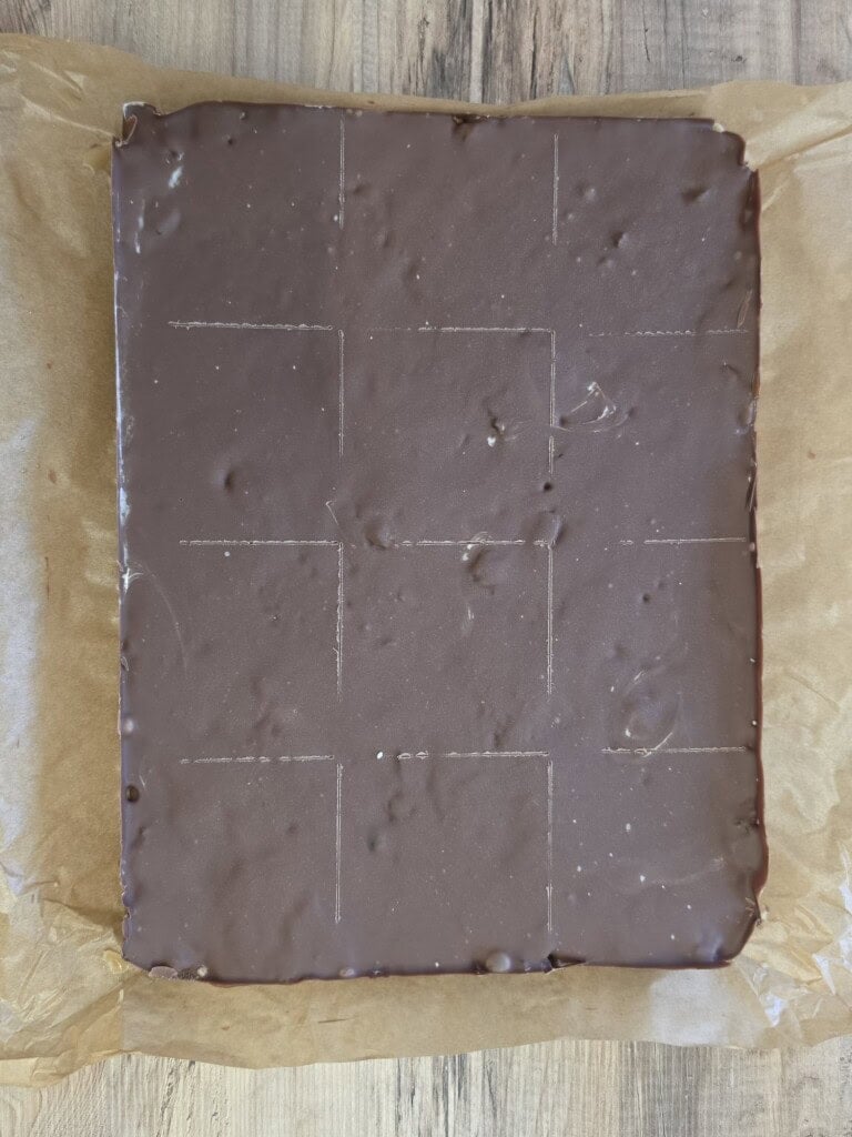 A rectangular block of chocolate resting on baking parchment, scored into a grid of nine squares.