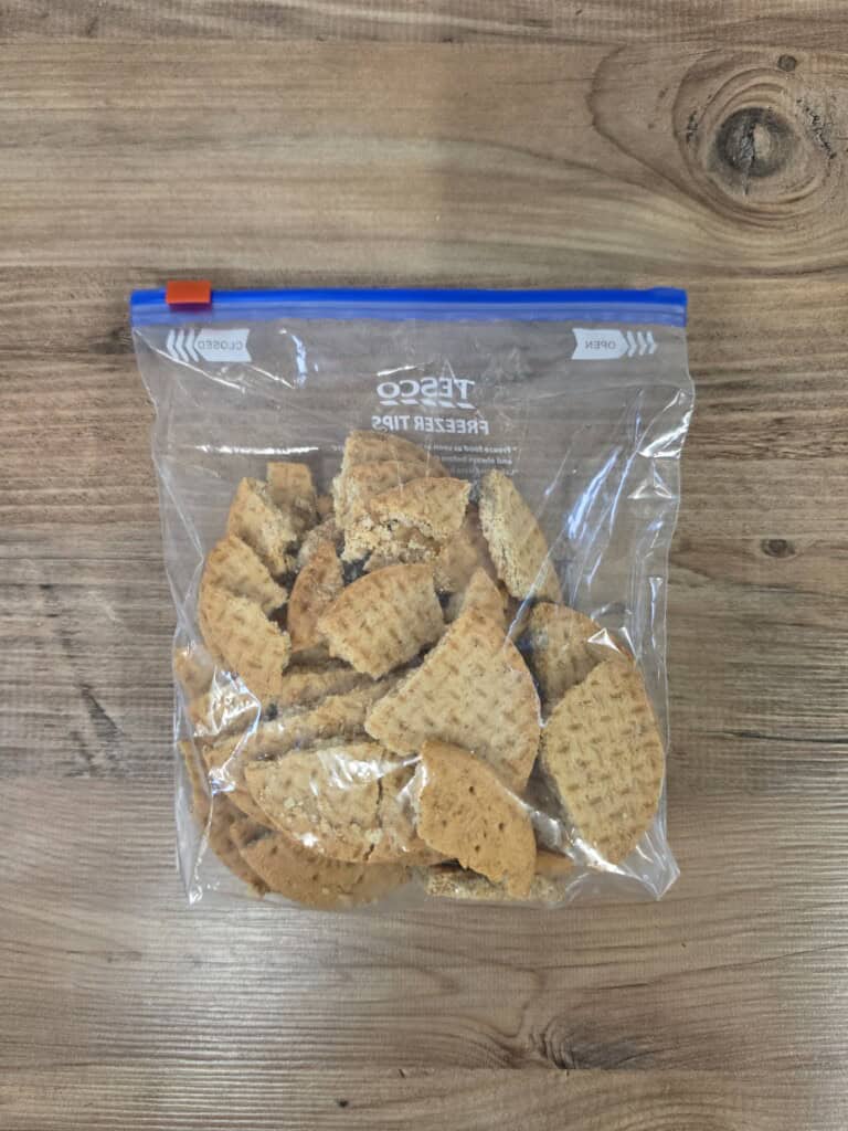 A plastic freezer bag filled with broken digestive biscuits sitting on a wooden surface.